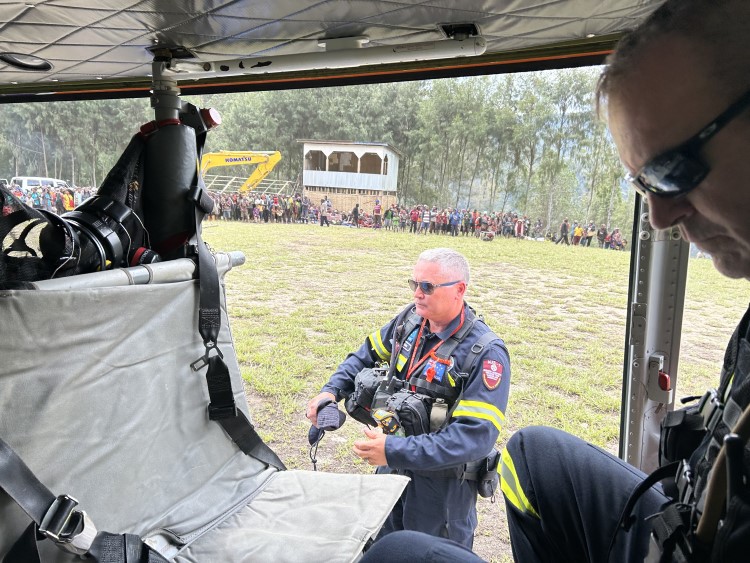 Looking out a helicopter door on arrival at a highland village oval where villagers watch from a distance